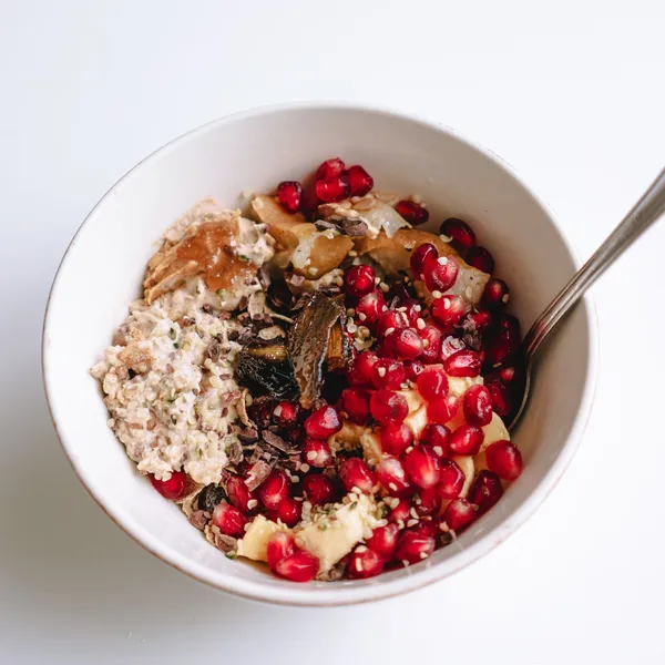 Oat breakfast bowl topped with pomegranate, nuts and fruit