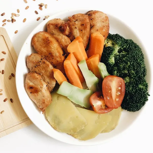 Grilled chicken with carrot, broccoli, sweet potato and tomato on a white plate